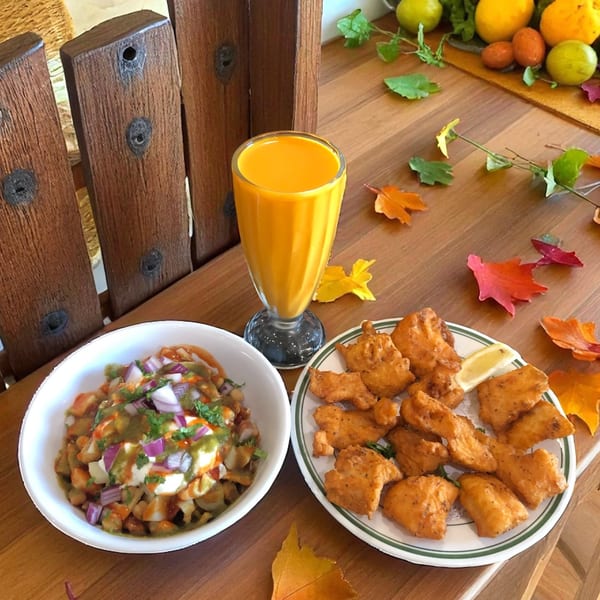 Indian appetizers: a bowl of chaat, a glass of mango lassi, and a plate of fried pakoras.