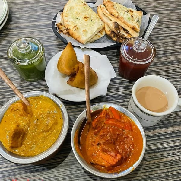 A table spread of Dhaba Indian Cuisine dishes including naan, samosas, curries, chutneys, and chai.