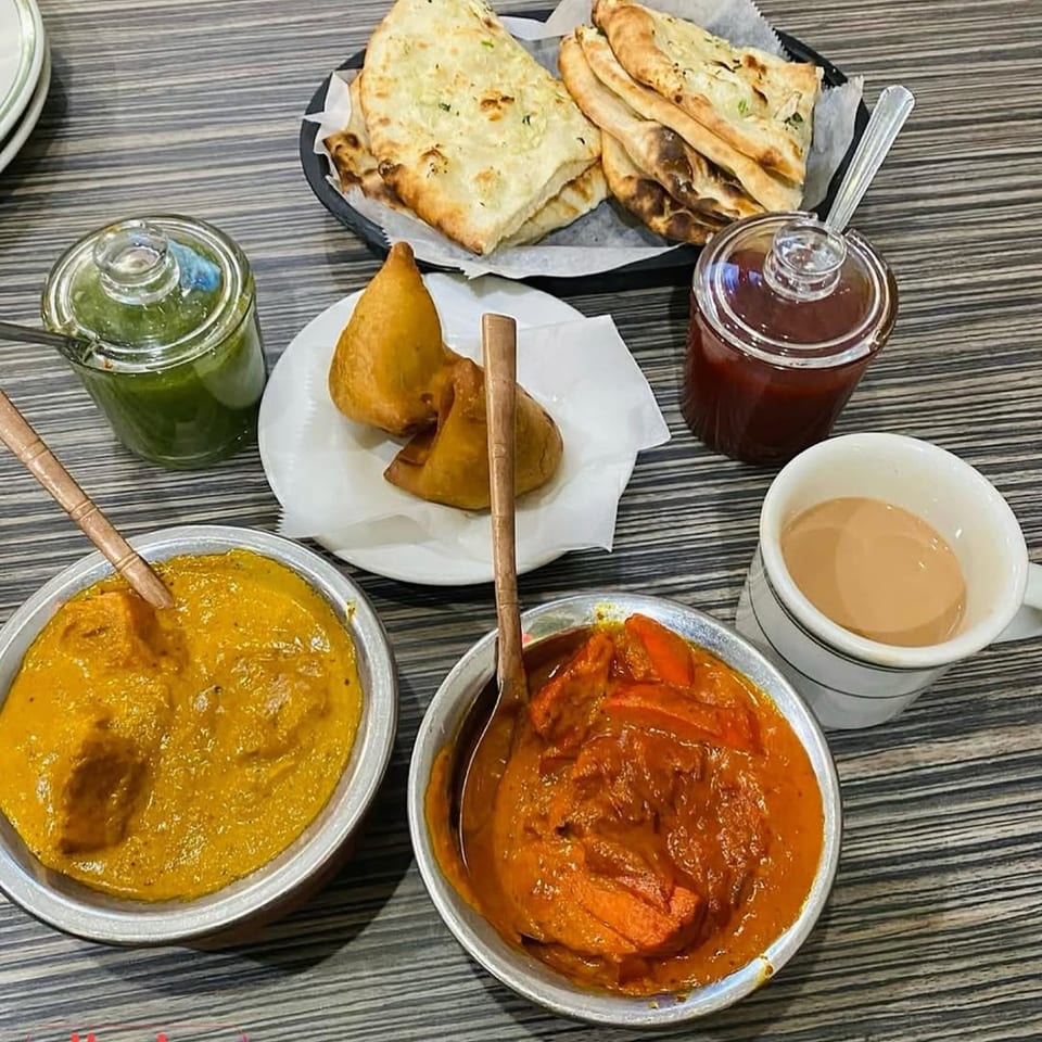 A table spread of Dhaba Indian Cuisine dishes including naan, samosas, curries, chutneys, and chai.