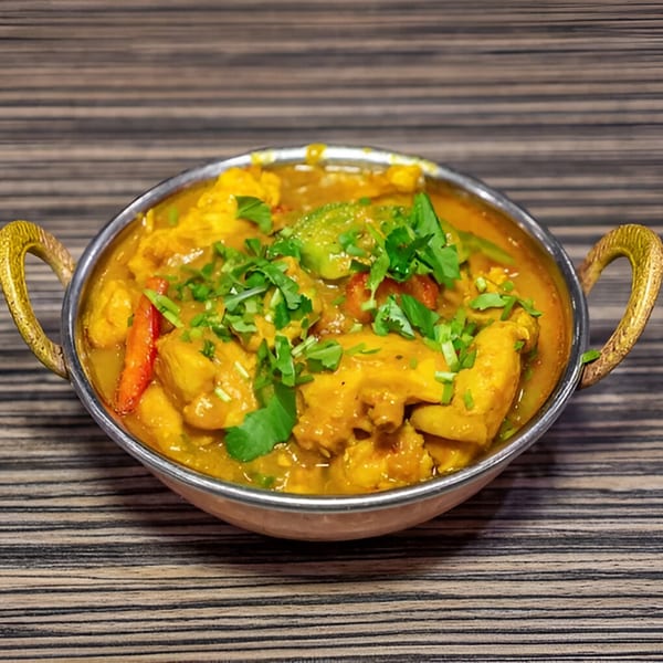 Dhaba Indian Cuisine's chicken curry with vegetables and cilantro in a traditional metal bowl.