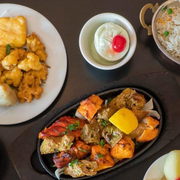 A Dhaba Indian Cuisine meal with mixed grill, pakoras, rice, and a dessert on a dark table.