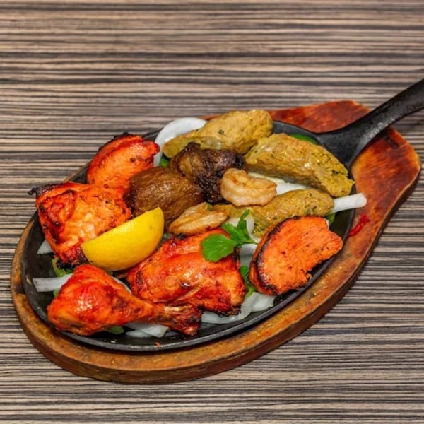 Indian mixed grill platter with tandoori chicken, seekh kebab, shrimp, and vegetables on a sizzling skillet.