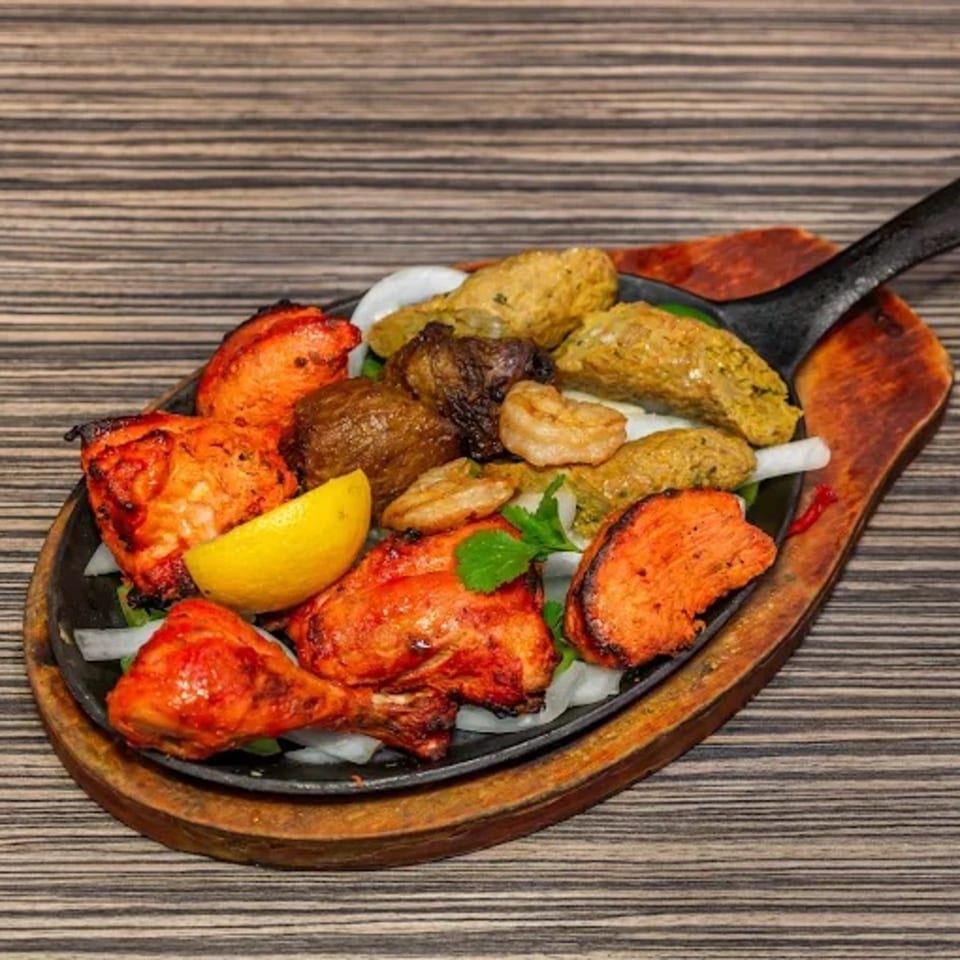 Indian mixed grill platter with tandoori chicken, seekh kebab, shrimp, and vegetables on a sizzling skillet.
