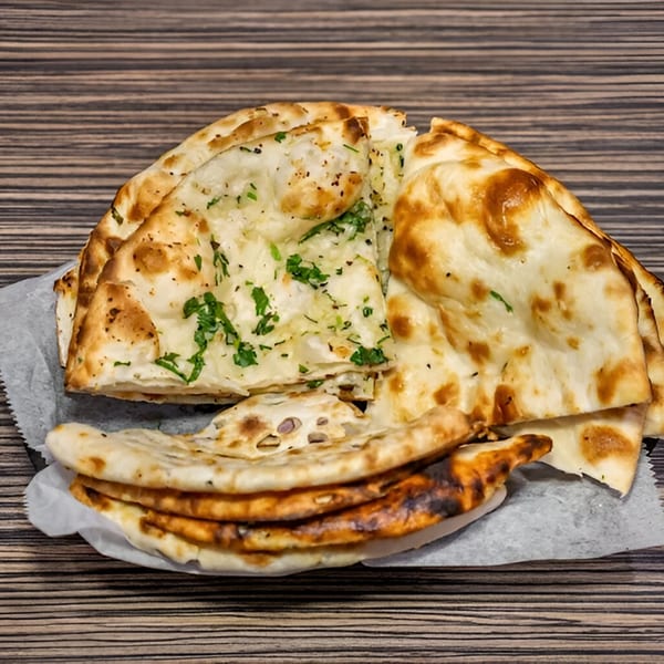 A basket of Dhaba Indian Cuisine naan bread, some topped with fresh green herbs, on a wooden table.