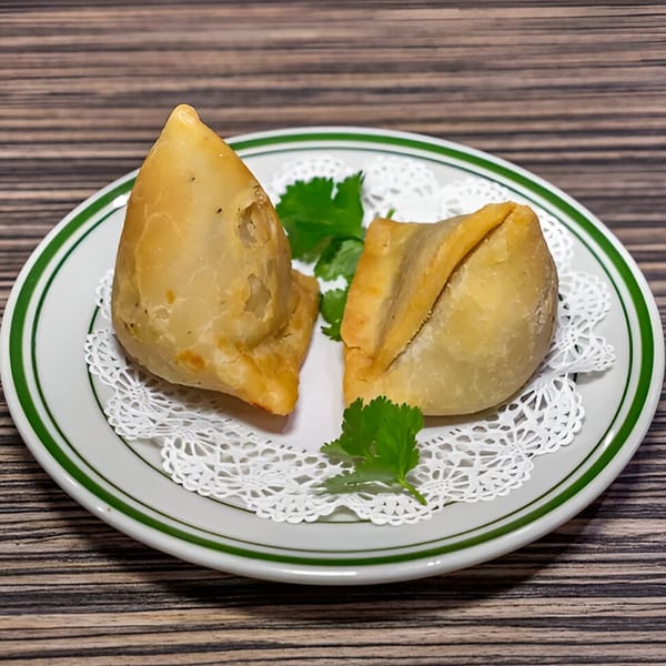Two golden-brown Dhaba Indian Cuisine samosas garnished with fresh cilantro on a white plate.