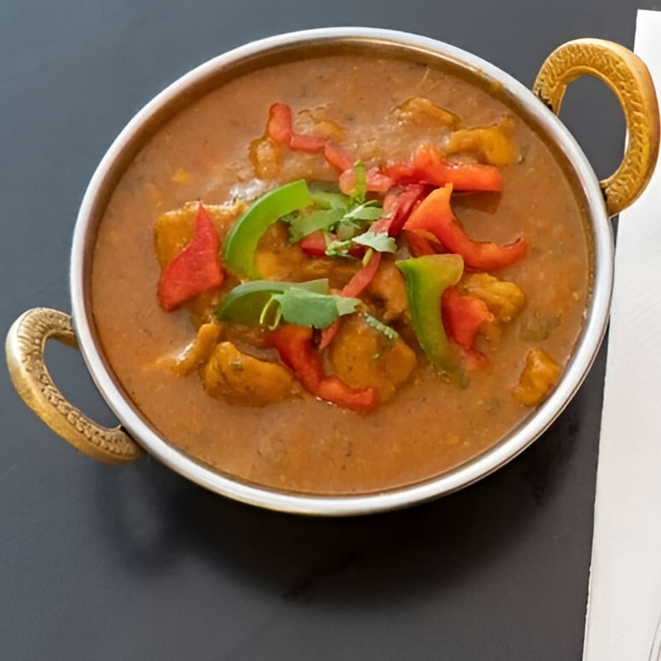 Dhaba Indian Cuisine's chicken curry in a metal bowl, garnished with red and green peppers and cilantro.