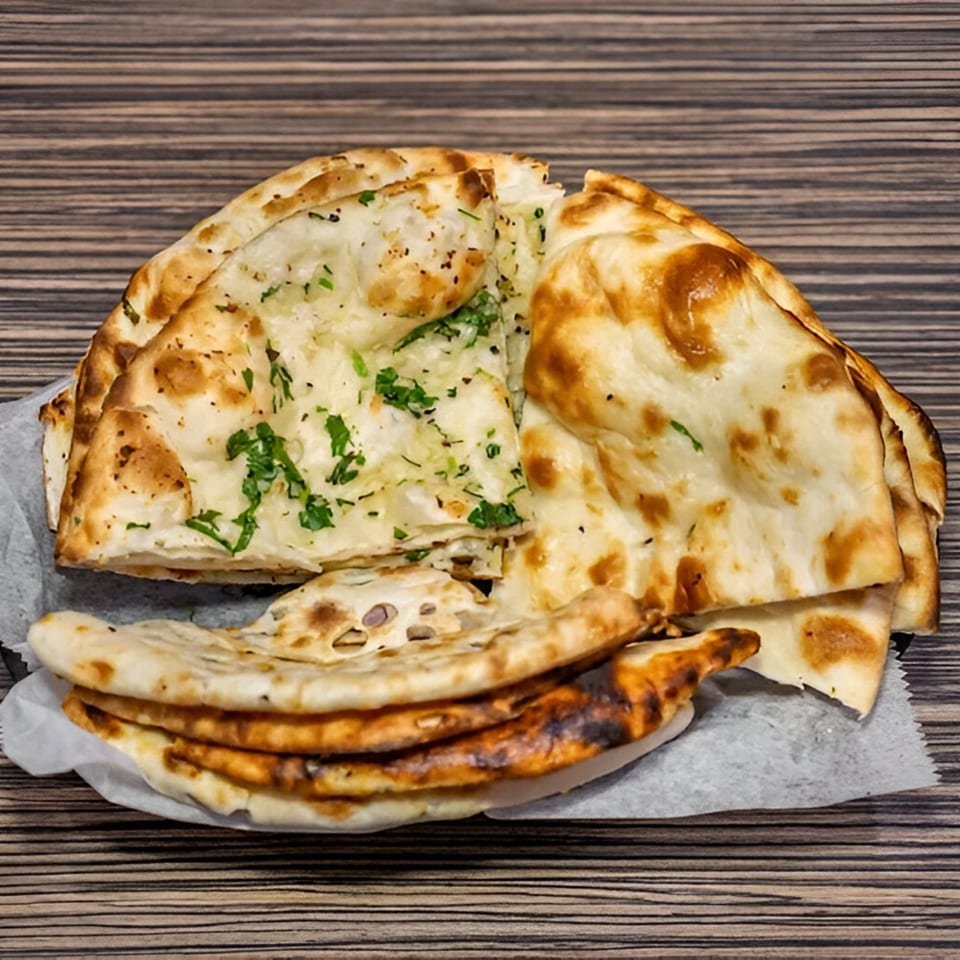 A basket of Dhaba Indian Cuisine's garlic naan and plain naan on a wooden table.